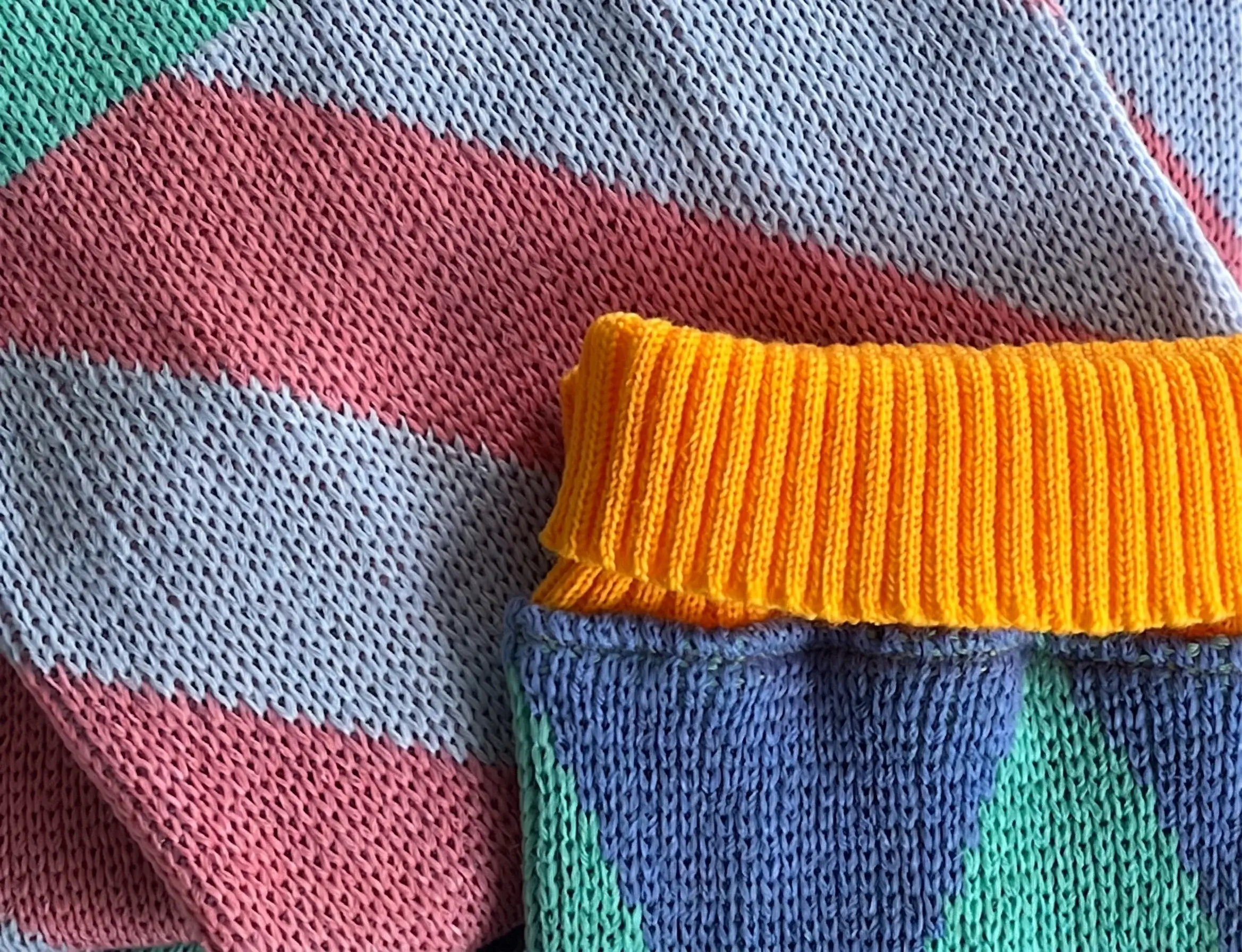 Acercamiento al tejido de dos suéteres en tonos pastel y un puño amarillo