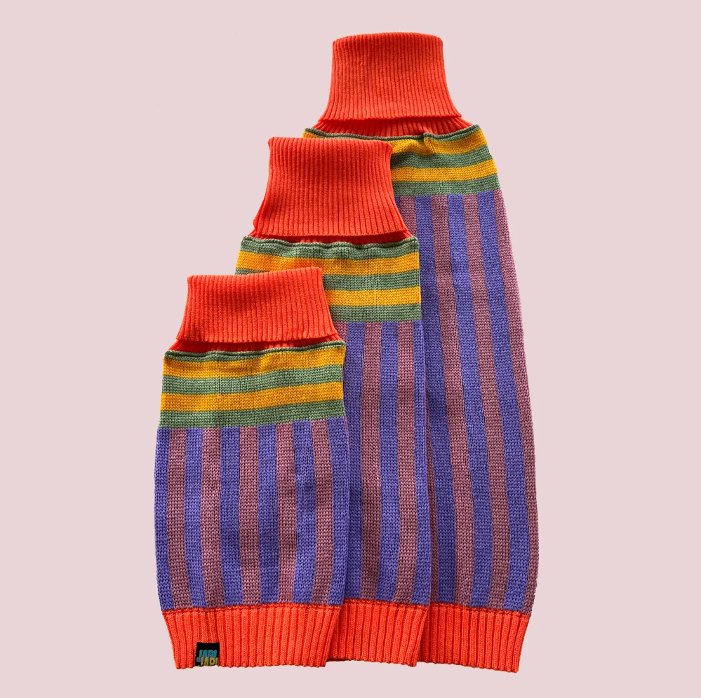 Tres tallas del suéter Japi Japi Elvis, tejido a rayas moradas y rosas con cuello coral, sobre fondo azul lavanda